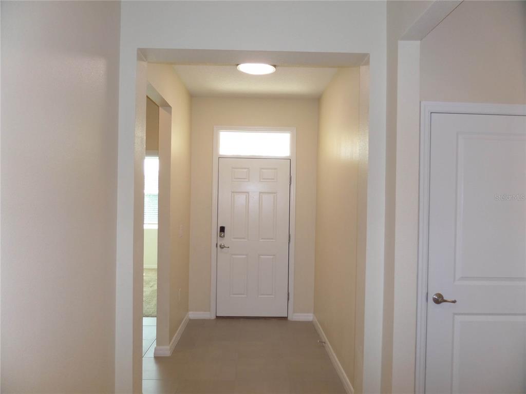 A bright entryway features a white front door, light-colored tile flooring, and beige walls — 7832 PENROSE PLACE, WILDWOOD, FL