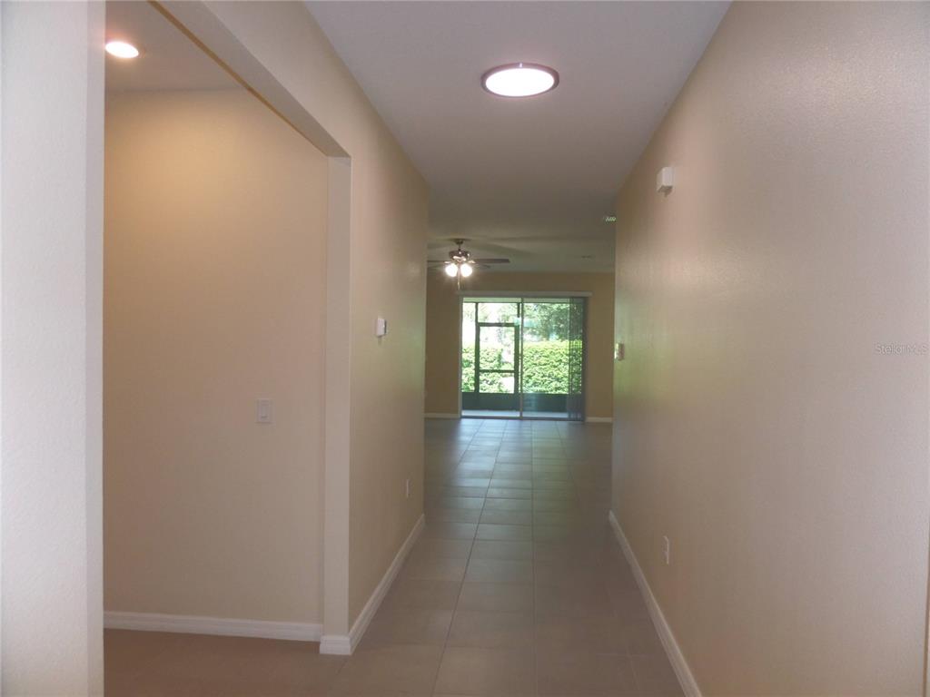 A tiled hallway leads to an open living area with a ceiling fan and sliding doors — 7832 PENROSE PLACE, WILDWOOD, FL