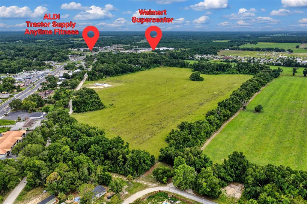 This is an aerial view of a large, undeveloped grassy field near commercial shopping centers — Block L NW 11TH DRIVE, CHIEFLAND, FL