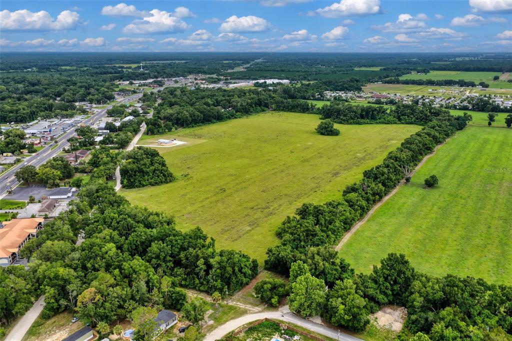 An aerial view shows a large, open grassy field bordered by trees and nearby roads — Block L NW 11TH DRIVE, CHIEFLAND, FL