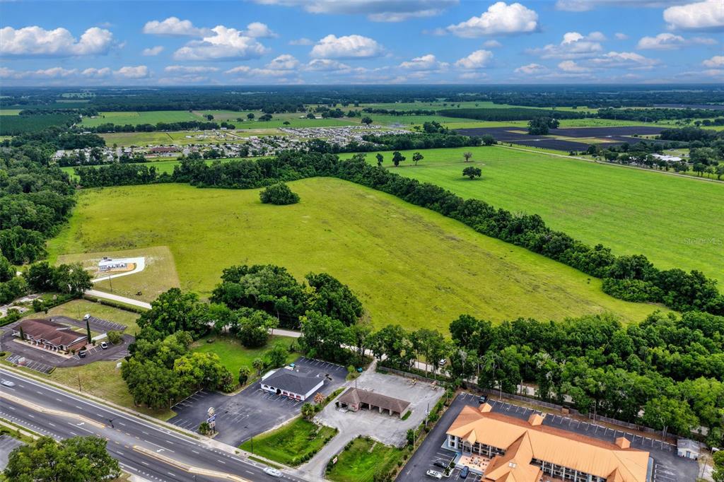 An aerial view shows a large grassy field adjacent to commercial buildings and a road — Block L NW 11TH DRIVE, CHIEFLAND, FL