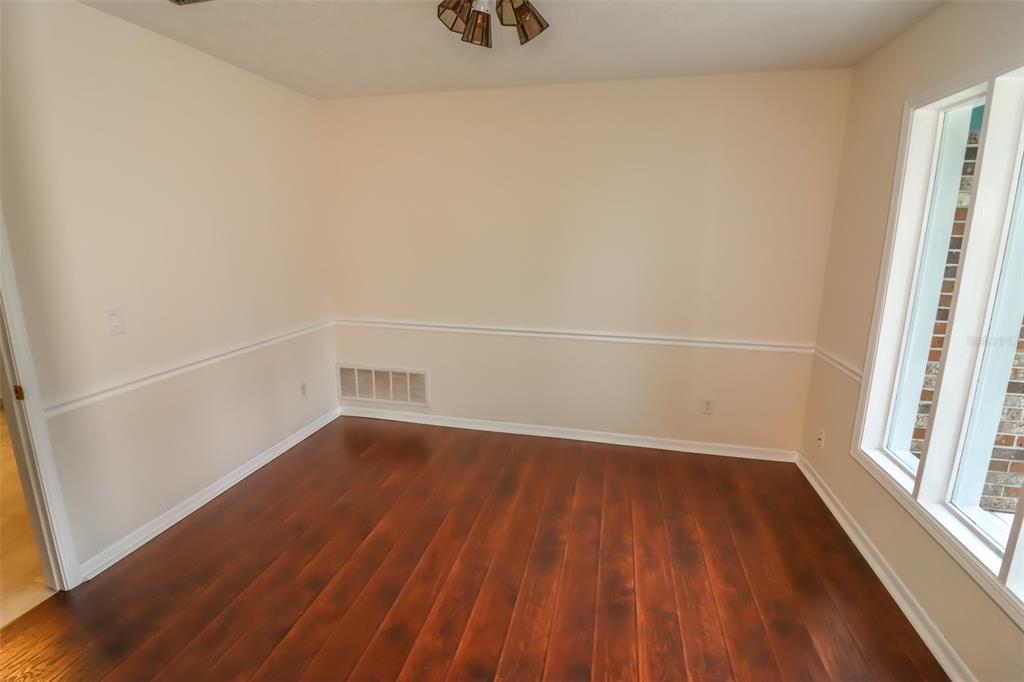An empty room with dark wood flooring, beige walls, chair rail molding, and large windows — 3442 RED OAK CIRCLE E, ORANGE PARK, FL