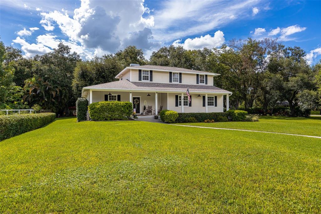 A two-story house with a covered front porch sits on a large, grassy lawn — 4691 LONG LAKE DRIVE, FORT MYERS, FL