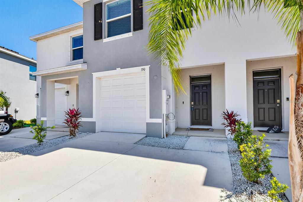 A two-story townhouse exterior features a white garage, two dark front doors, and landscaping — 350 MANGROVE SHADE CIRCLE, APOLLO BEACH, FL