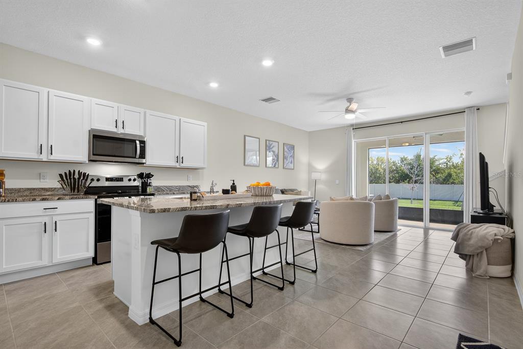 A kitchen with white cabinets and a granite island overlooks a living area with sliding doors — 350 MANGROVE SHADE CIRCLE, APOLLO BEACH, FL
