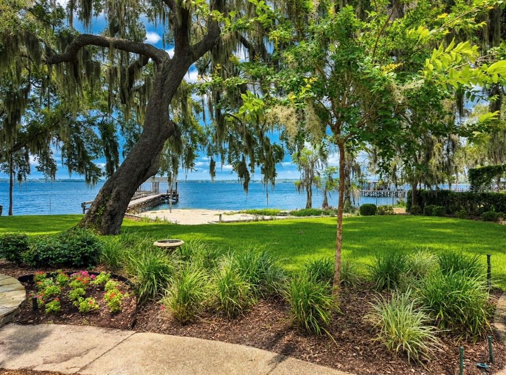 A grassy backyard leads to a sandy beach and a wooden dock on a lake — 1341 W LAKESHORE DRIVE, CLERMONT, FL