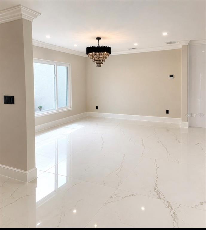 A bright, empty room features white marble-look tile flooring, a dark chandelier, and crown molding — 1341 W LAKESHORE DRIVE, CLERMONT, FL