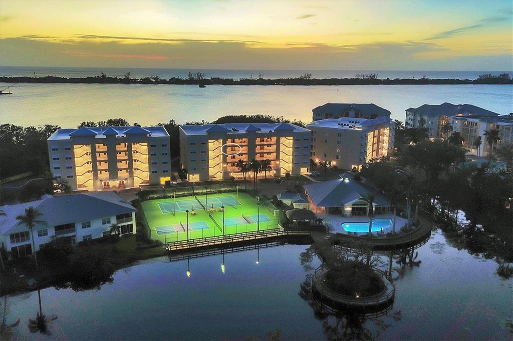 An aerial view shows apartment buildings, tennis courts, and a swimming pool near the water — 260 HIDDEN BAY DRIVE UNIT 402, OSPREY, FL