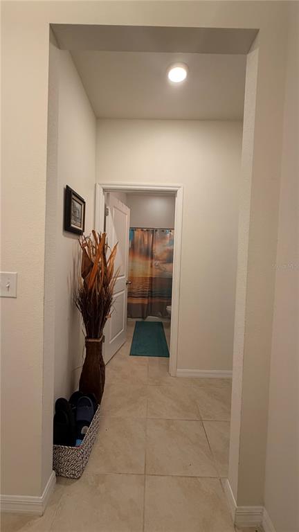 A hallway with tile flooring leads to a bathroom featuring a sunset-themed shower curtain — 6403 DEVESTA LOOP, PALMETTO, FL