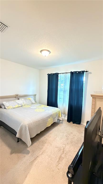 A bedroom features a bed with a patterned quilt, dark curtains, and beige carpeting — 6403 DEVESTA LOOP, PALMETTO, FL