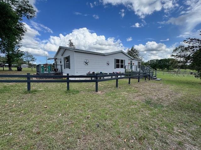 A light-colored manufactured home sits behind a black wooden fence under a cloudy sky — 19231 NW HIGHWAY 335, WILLISTON, FL