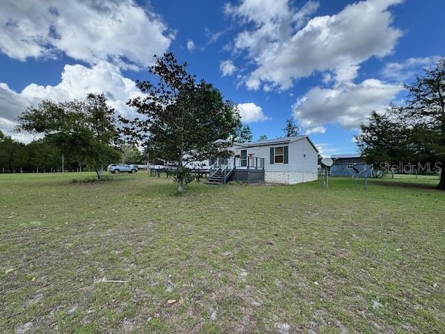 A single-story manufactured home sits on a large, grassy lot under a cloudy blue sky — 19231 NW HIGHWAY 335, WILLISTON, FL