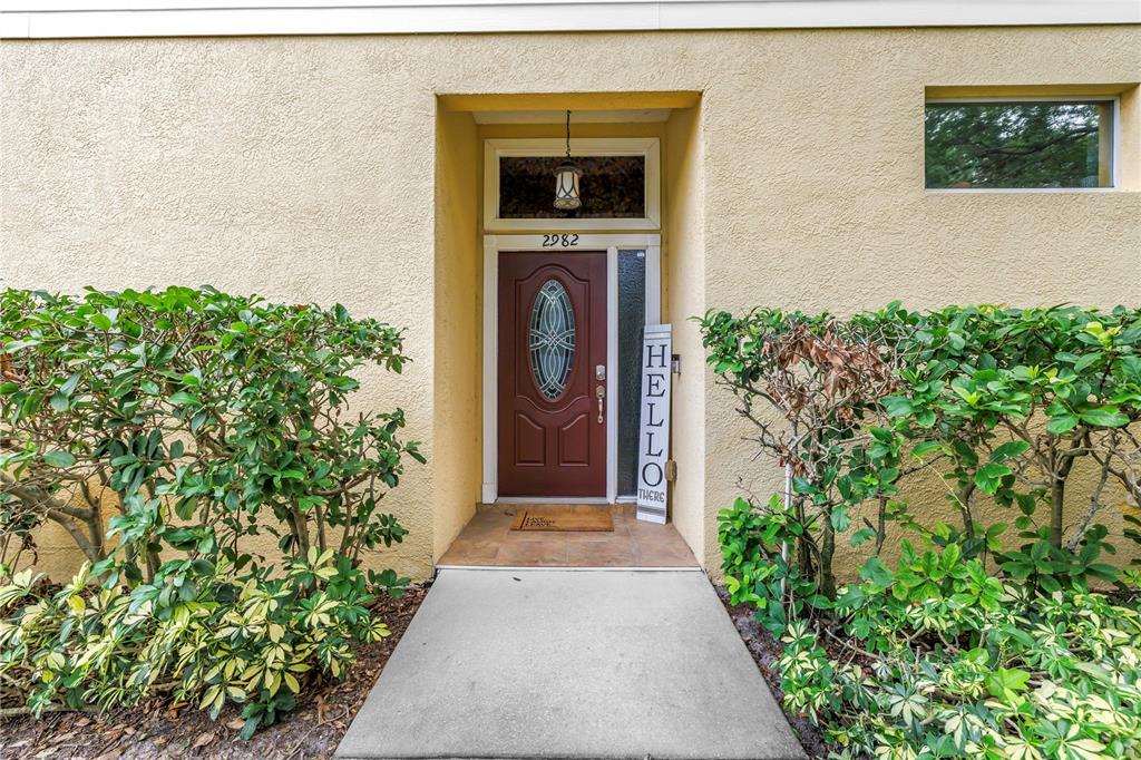 A front entrance with a red door, a "Hello" sign, and surrounding green bushes — 2982 ESTANCIA PLACE, CLEARWATER, FL