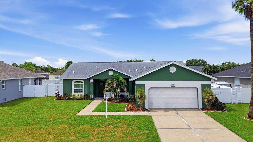 A single-story green house with a two-car garage and a white fence under a blue sky — 9301 71ST AVENUE E, PALMETTO, FL