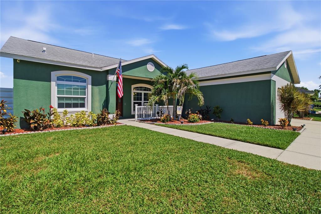 A green single-story house features a front porch, a flag, and a landscaped lawn — 9301 71ST AVENUE E, PALMETTO, FL