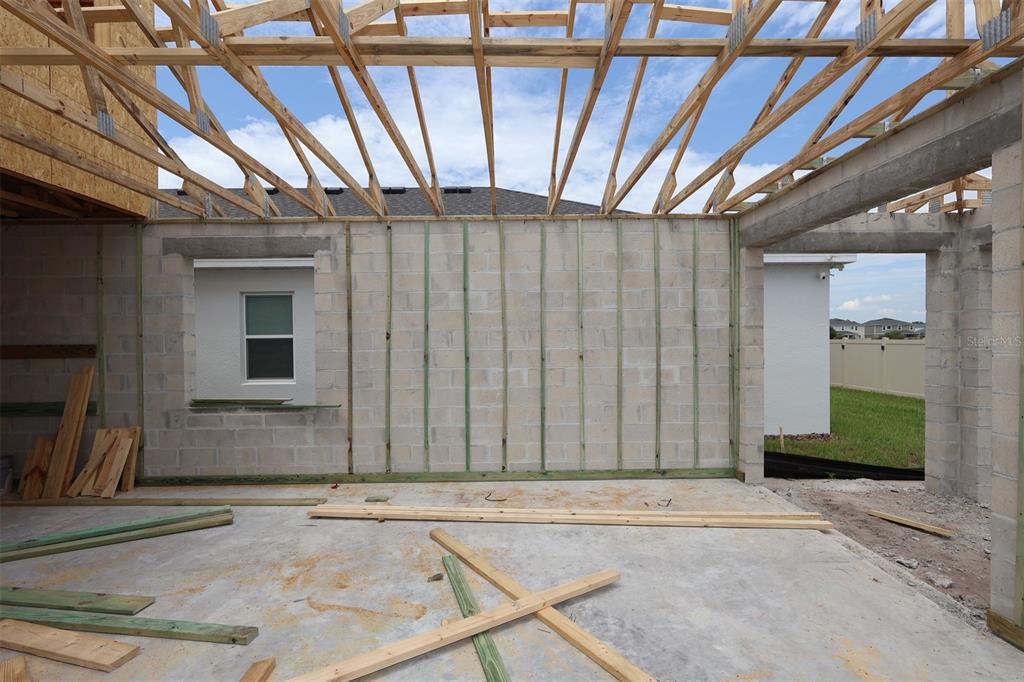 An unfinished room with concrete block walls, exposed roof trusses, and scattered construction lumber — 6777 YELLOW WARBLER BEND, ST CLOUD, FL