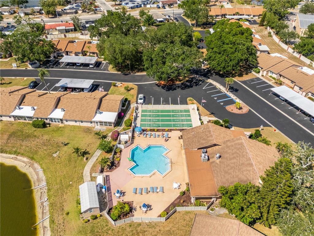 An aerial view shows a community swimming pool, shuffleboard courts, and adjacent residential buildings — 3801 SAILMAKER LANE, HOLIDAY, FL