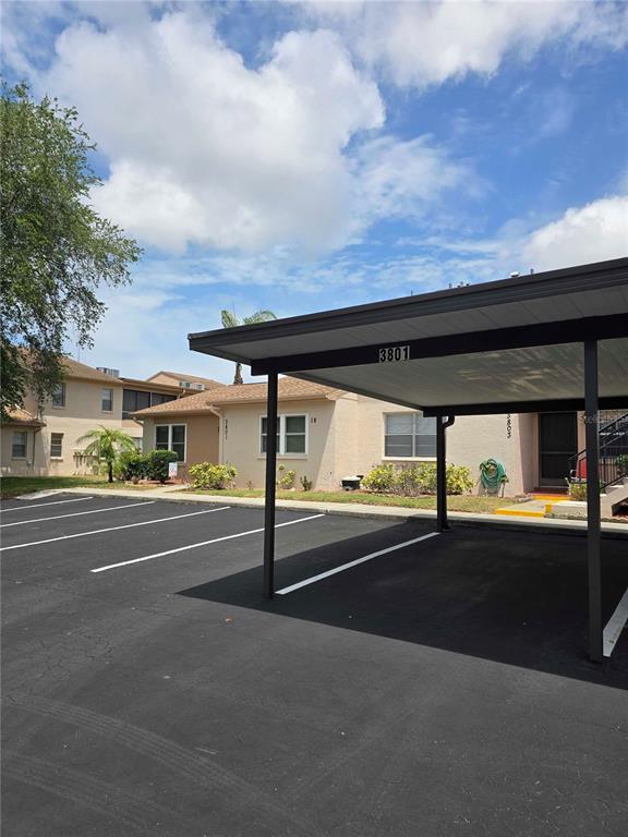 A covered carport sits in front of a tan residential building with a parking lot — 3801 SAILMAKER LANE, HOLIDAY, FL