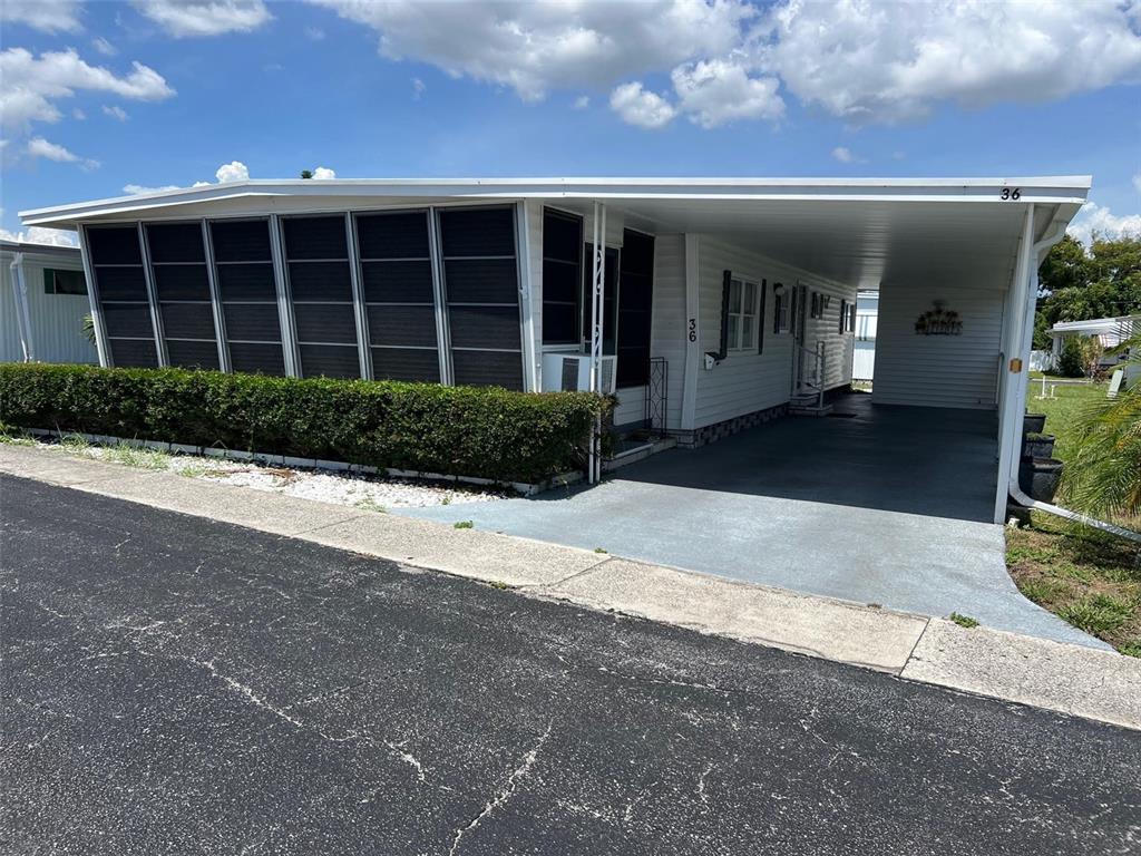 A white mobile home features a screened-in porch, a carport, and a manicured hedge — 36 THATCH PALM STREET E, LARGO, FL