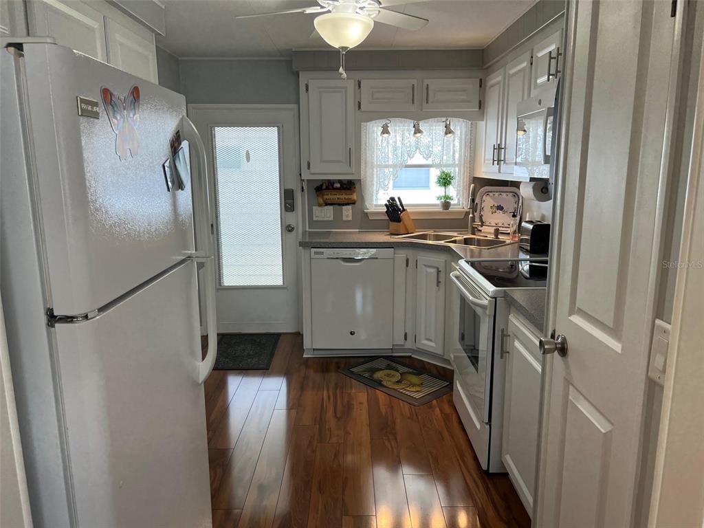 A kitchen features white cabinets, stainless steel appliances, and wood-look flooring — 36 THATCH PALM STREET E, LARGO, FL