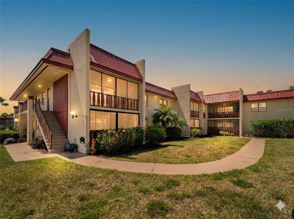A two-story apartment building with a red metal roof and exterior staircases at sunset — 72 BOUNDARY BOULEVARD UNIT 226, ROTONDA WEST, FL