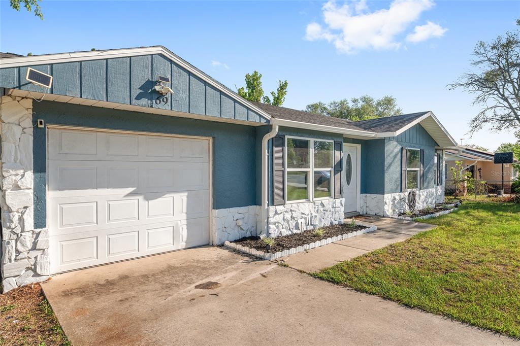 A blue house with white stone accents and a single-car garage under a blue sky — 69 SAPPHIRE ROAD, OCALA, FL