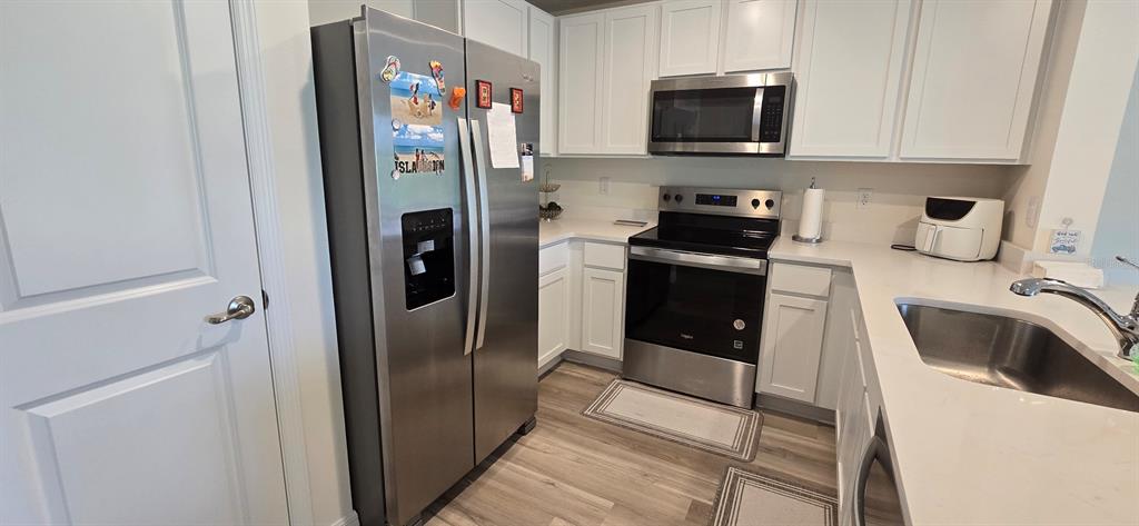 A kitchen features white cabinets, stainless steel appliances, light countertops, and wood-look flooring — 8375 GOWER TRAIL, WILDWOOD, FL