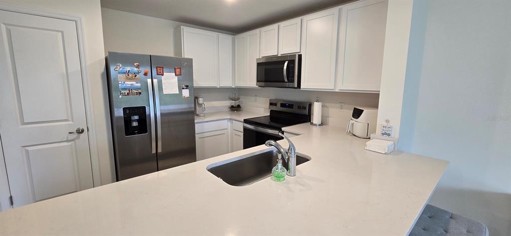 A kitchen features white cabinets, stainless steel appliances, and a white quartz countertop island — 8375 GOWER TRAIL, WILDWOOD, FL