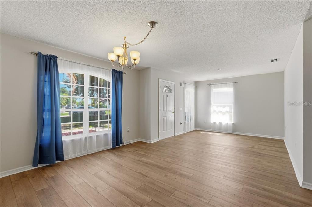 A bright living room features light wood-look flooring, white walls, and a central chandelier — 372 LAKE DAISY CIR, WINTER HAVEN, FL