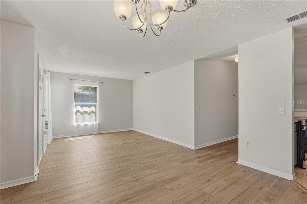 An empty room with light wood-look flooring, white walls, and a multi-light chandelier — 372 LAKE DAISY CIR, WINTER HAVEN, FL