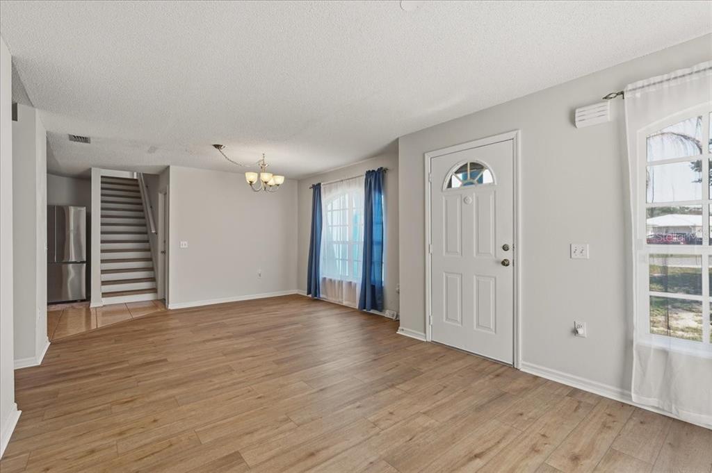 An empty living room with light wood flooring, a front door, and a staircase — 372 LAKE DAISY CIR, WINTER HAVEN, FL