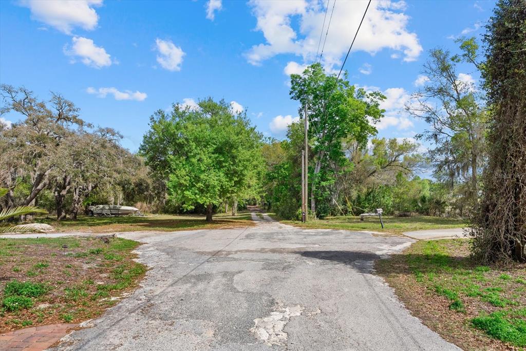 A paved road leads toward a wooded area with a boat parked on the left — INDALE DRIVE, NEW PORT RICHEY, FL
