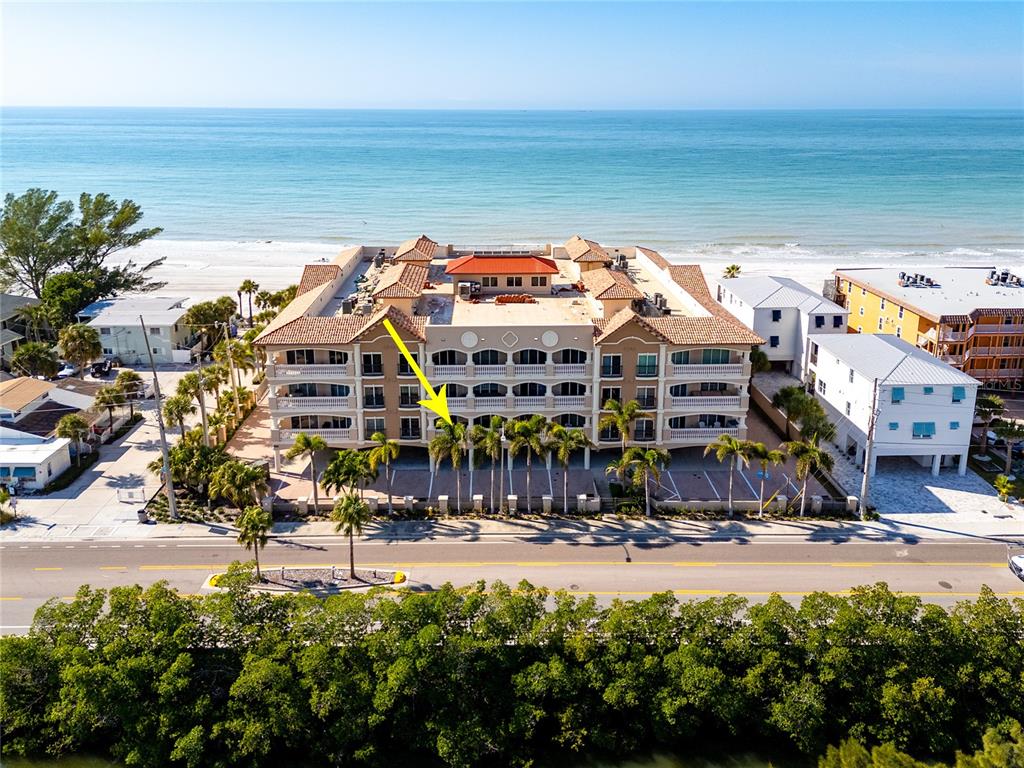 An aerial view shows a multi-story beachfront condominium building with a yellow arrow pointing downward — 604 GULF BOULEVARD UNIT 207, INDIAN ROCKS BEACH, FL