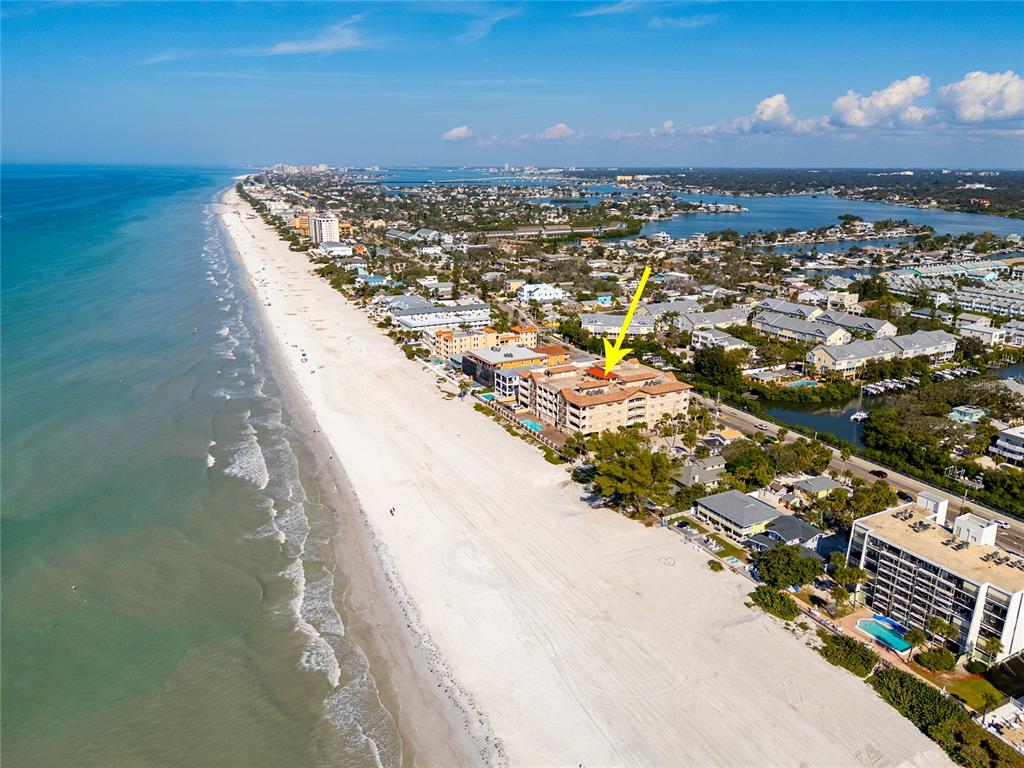 An aerial view shows a beachfront condominium complex with a yellow arrow pointing toward it — 604 GULF BOULEVARD UNIT 207, INDIAN ROCKS BEACH, FL