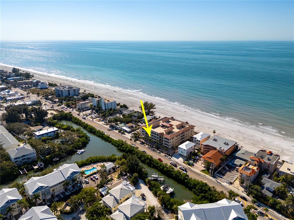 An aerial view shows a multi-story beachfront condominium building marked by a yellow arrow — 604 GULF BOULEVARD UNIT 207, INDIAN ROCKS BEACH, FL