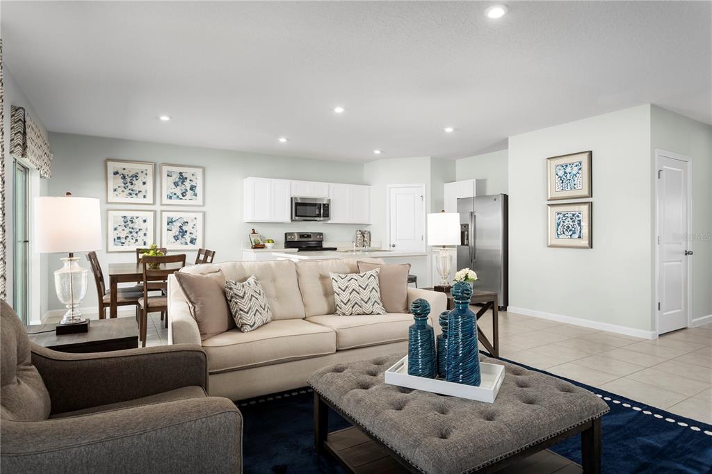 An open-concept living room and kitchen featuring a beige sofa, gray ottoman, and stainless appliances — 8884 WILDFLOWER FIELD LANE, WILDWOOD, FL