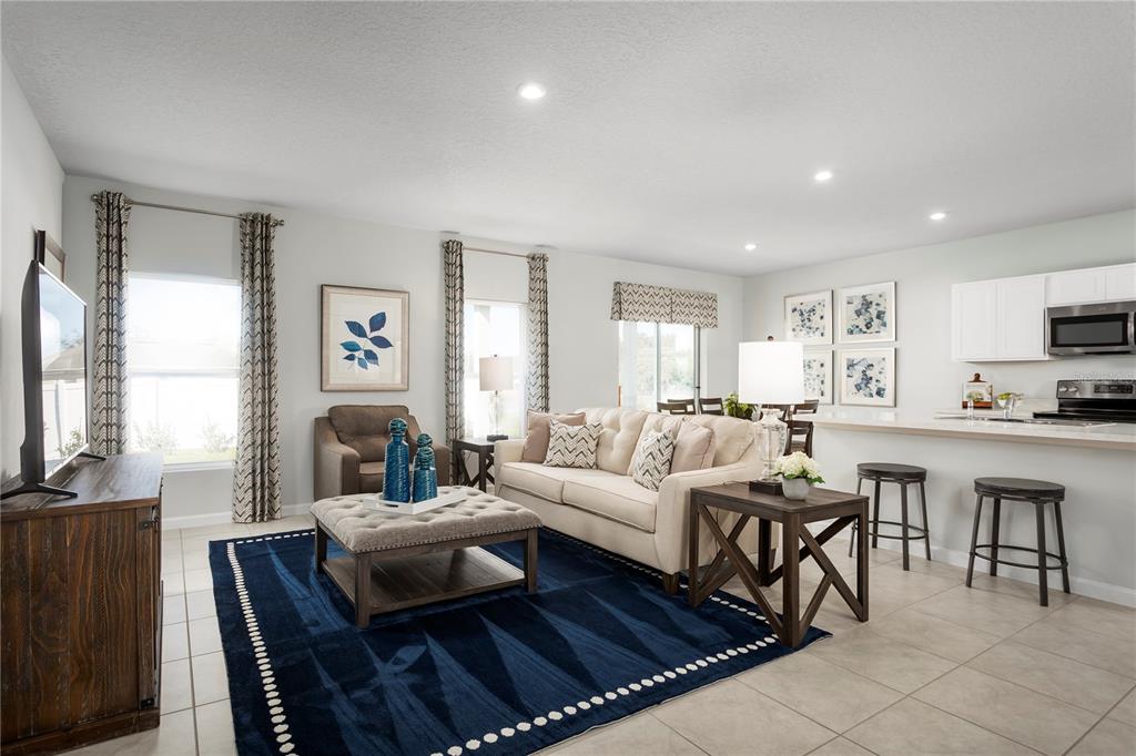A living room features a blue area rug, beige sofa, and an open kitchen area — 8884 WILDFLOWER FIELD LANE, WILDWOOD, FL
