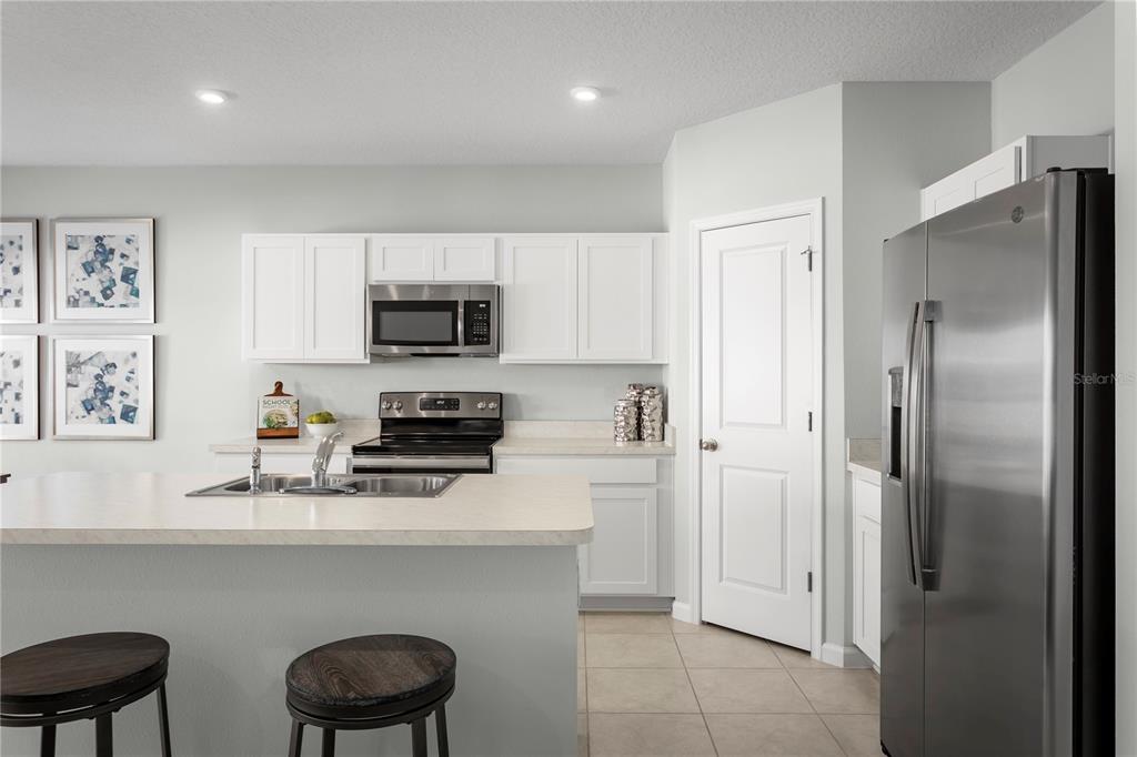 A kitchen features white cabinets, stainless steel appliances, a center island, and tile flooring — 8884 WILDFLOWER FIELD LANE, WILDWOOD, FL