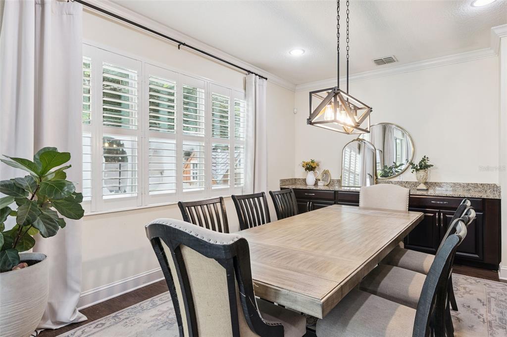 A dining room features a wooden table, upholstered chairs, plantation shutters, and a dark buffet — 2205 PICKFORD CIRCLE, APOPKA, FL