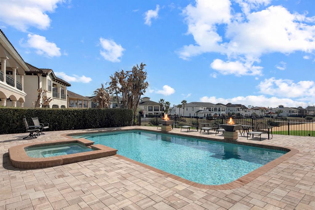 A swimming pool and hot tub sit on a paved patio with two fire bowls — 451 MUIRFIELD LOOP, REUNION, FL