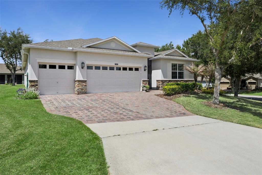 A single-story house with a three-car garage, stone accents, and a brick paver driveway — 2892 SANDY CAY STREET, CLERMONT, FL