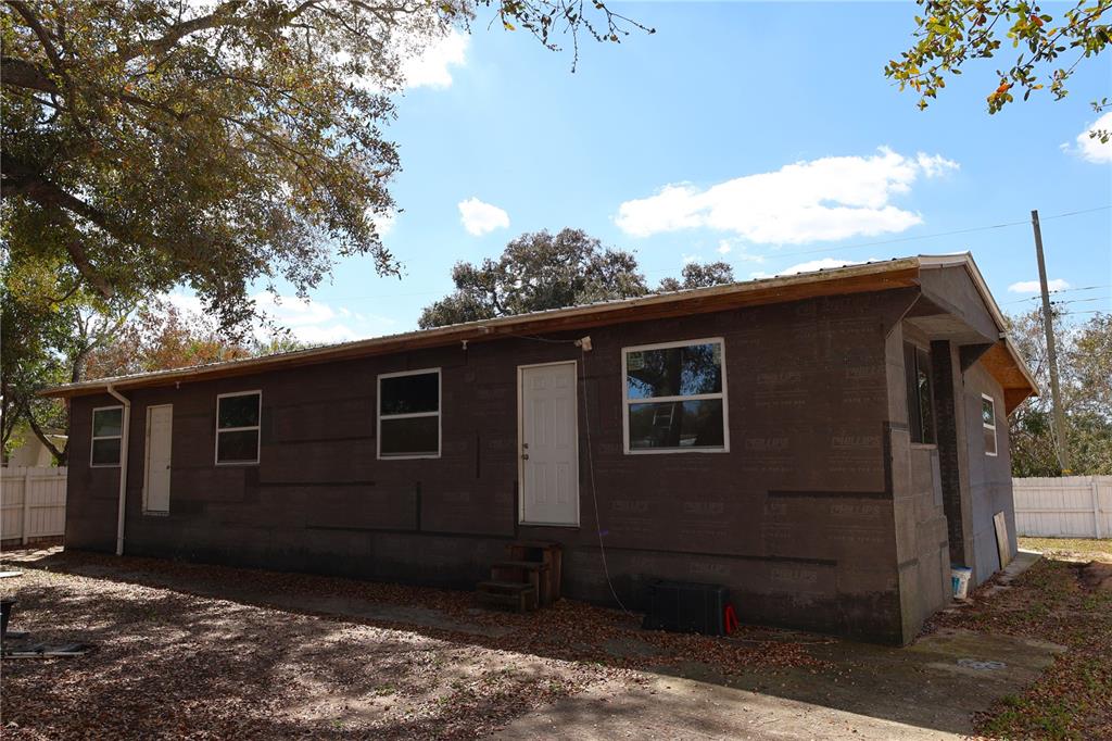 The exterior of a single-story house features dark sheathing, several windows, and a white door — 6991 ASH DRIVE, COCOA, FL