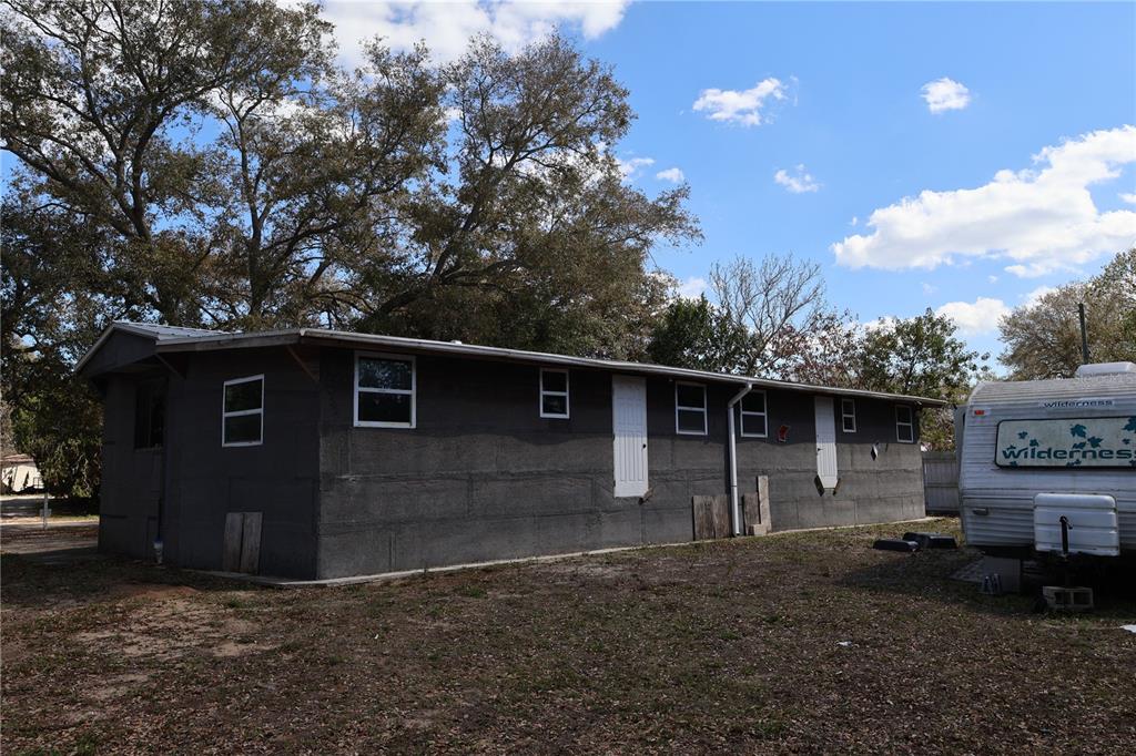 A dark gray, single-story exterior structure sits on a dirt lot next to a camper — 6991 ASH DRIVE, COCOA, FL