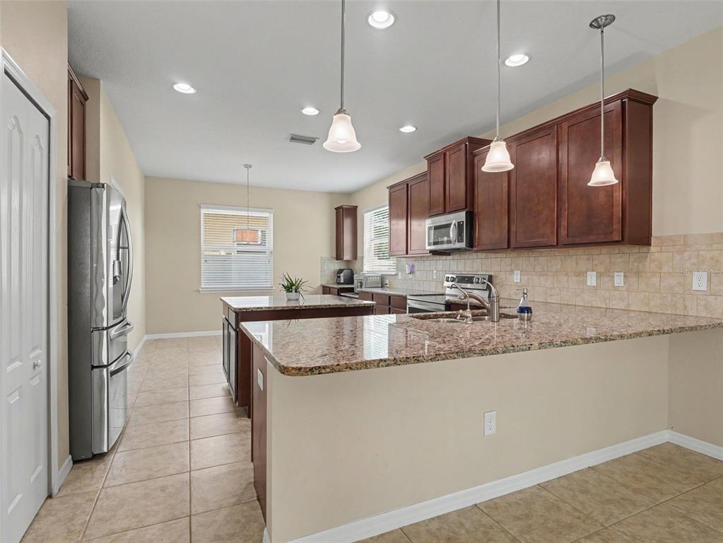 A kitchen features dark wood cabinets, granite countertops, stainless steel appliances, and tile flooring — 10413 AVIAN FORREST DRIVE, RIVERVIEW, FL