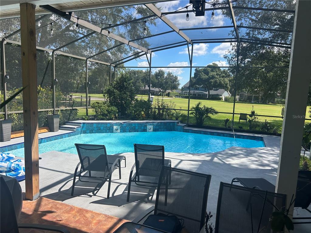A swimming pool with a blue tiled wall sits inside a screened-in patio enclosure — 2435 SWEETWATER COUNTRY CLUB PLACE DRIVE, APOPKA, FL