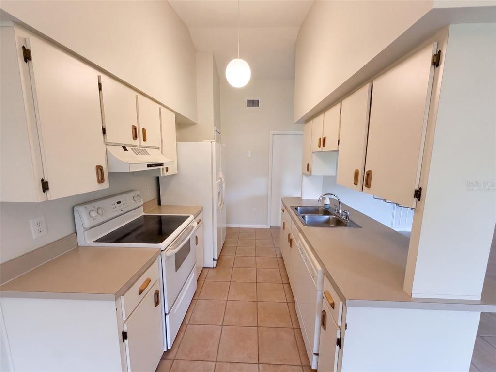 A galley-style kitchen features white cabinets, tan countertops, white appliances, and light-colored tile flooring — 1061 HUNT STREET NW, PALM BAY, FL