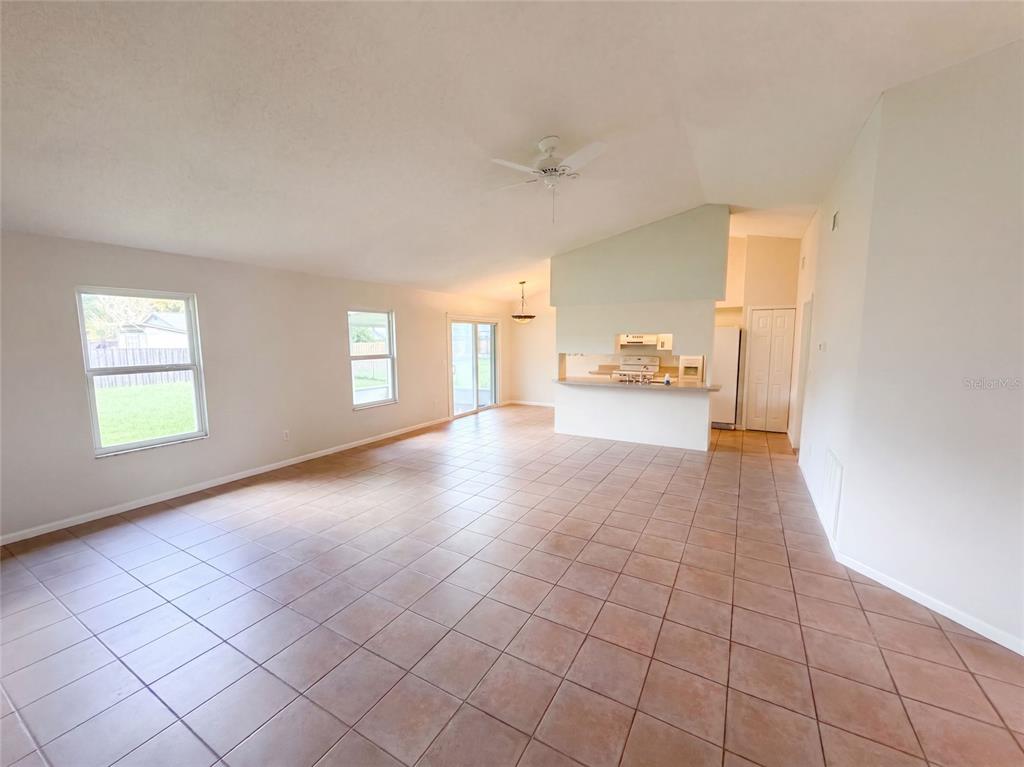 An open-concept living and dining area features vaulted ceilings, tile flooring, and a kitchen pass-through — 1061 HUNT STREET NW, PALM BAY, FL