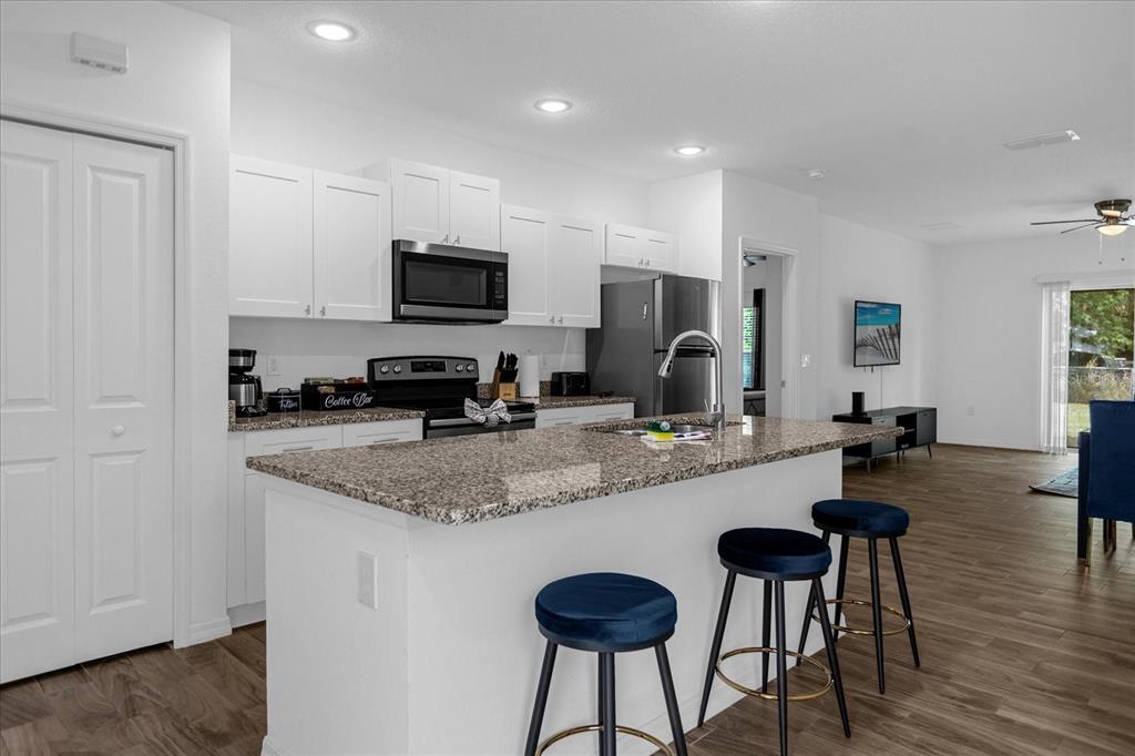 A kitchen with white cabinets, granite countertops, and an island with three blue bar stools — 97 N GOLDWYN AVENUE, ORLANDO, FL