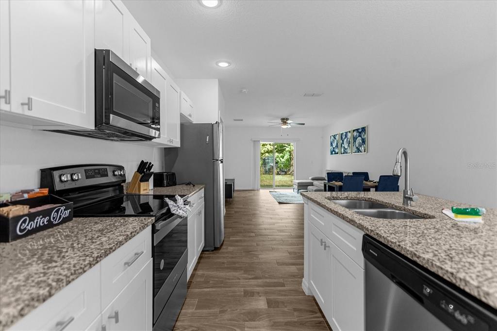 A kitchen with white cabinets, granite countertops, and stainless steel appliances opens to a living area — 97 N GOLDWYN AVENUE, ORLANDO, FL