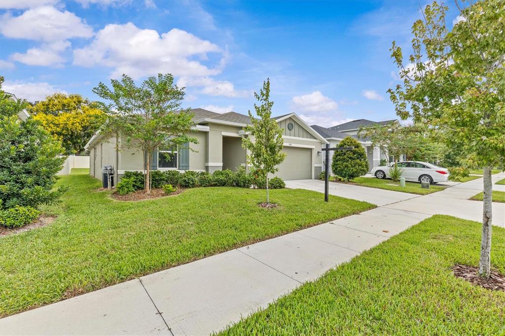 A hallway with light wood-look flooring leads to a living area with a gray sofa — 9972 MESIC WOODS AVENUE, SEFFNER, FL